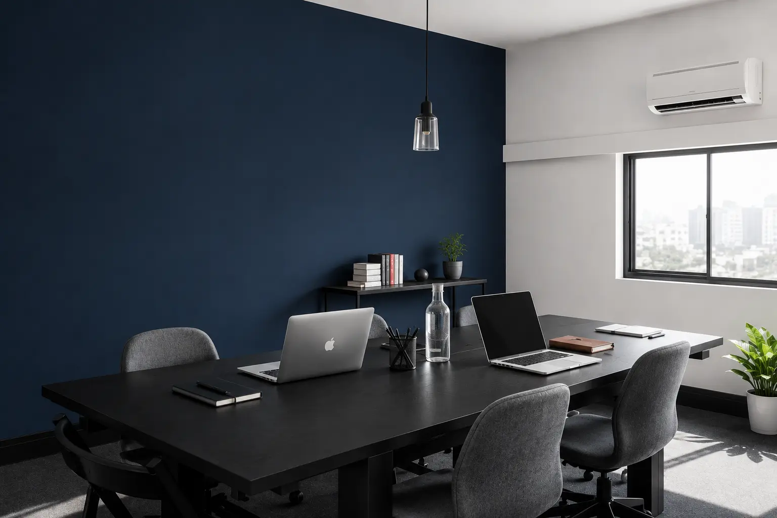 Modern minimalist office conference room with a black meeting table, ergonomic gray chairs, laptops, indoor plants, and a navy-blue accent wall, illuminated by natural light from a large window.